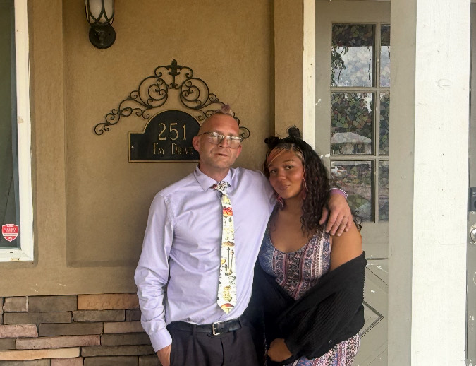 Jeremy Long and Jazzmyn Busby, the founders of Nexus to Hope, standing together and smiling beneath the 251 Fay Drive address plaque on the tan exterior of the residence